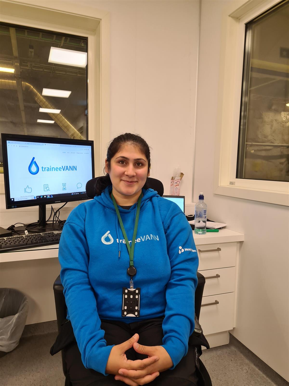 Smilende dame i blå hettegenser sitter foran pc - Klikk for stort bilde